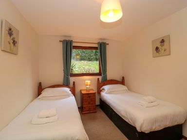 A bedroom with two single beds a nightstand and a window with curtains at The Oak Lodge near Lyme Regis