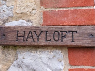 A wooden sign engraved with the words HAY LOFT mounted on a stone and brick wall at The Hayloft Cottage Apartment near Lyme Regis