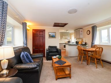 A living room with black leather sofa and armchair a wooden coffee table and dining table with chairs at The Hayloft Cottage Apartment near Lyme Regis
