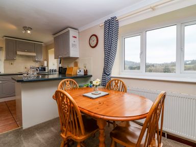 A dining area with a wooden table and chairs next to a window and a kitchen counter at The Hayloft Cottage Apartment near Lyme Regis