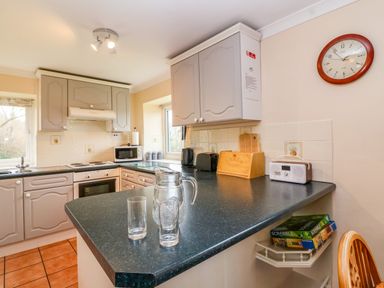 A kitchen with grey cabinets a black countertop a microwave a bread box a clock and board games on a shelf at The Hayloft Cottage Apartment near Lyme Regis