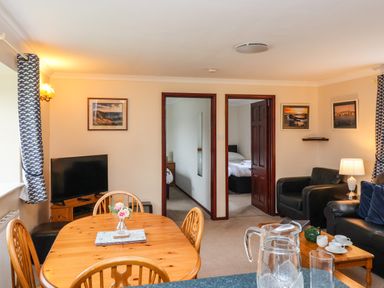 A living room with a wooden dining table and chairs a television and black armchairs at The Hayloft Cottage Apartment near Lyme Regis