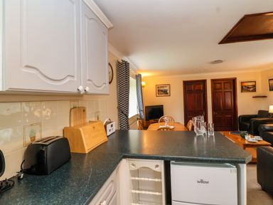 A kitchen counter with toaster bread box and water jug facing a dining table and living room at The Hayloft Cottage Apartment near Lyme Regis