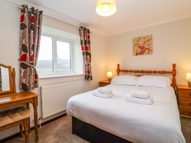A bedroom with a double bed and bedside tables with lamps and a dressing table near a window at The Hayloft Cottage Apartment near Lyme Regis