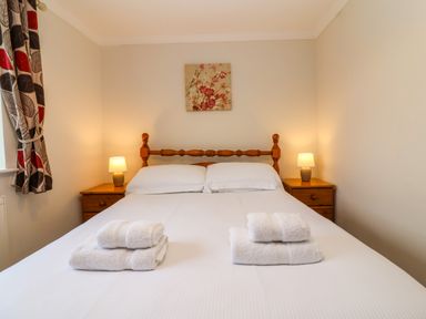 A bedroom with a double bed two bedside tables with lamps floral curtains and a painting at The Hayloft Cottage Apartment near Lyme Regis