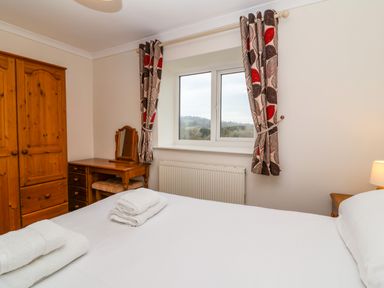 A bedroom with a bed with white linens wooden wardrobe dressing table and patterned curtains at The Hayloft Cottage Apartment near Lyme Regis