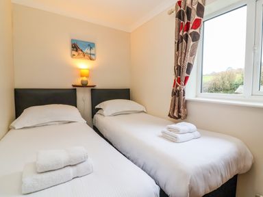 A bedroom with two single beds with white linens and towels on them a small lamp on a wall shelf between the beds and a window with patterned curtains at The Hayloft Cottage Apartment near Lyme Regis