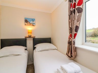 A bedroom with two single beds a wall lamp and a window with patterned curtain at The Hayloft Cottage Apartment near Lyme Regis