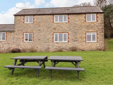 Stone house with six windows and two wooden picnic tables on grass near Lyme Regis