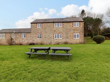 A stone house with white windows and two picnic tables on a grassy lawn at The Hayloft Cottage Apartment near Lyme Regis