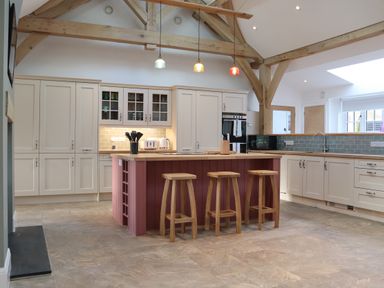 A kitchen with an island and three wooden stools under exposed beams at The Anchorage @ Nables Farm in Upper Seagry