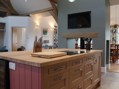 A kitchen island with a knife block and cooking utensils in a kitchen with a mounted television and dining area at The Anchorage @ Nables Farm in Upper Seagry
