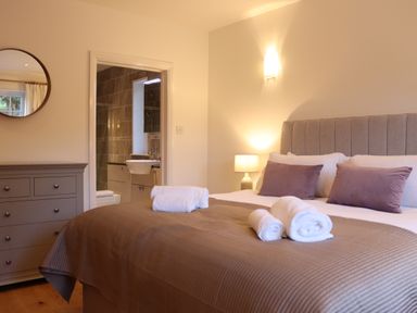 A bedroom with a bed pillows lamps and towels next to a dresser and an en suite bathroom at The Anchorage @ Nables Farm in Upper Seagry