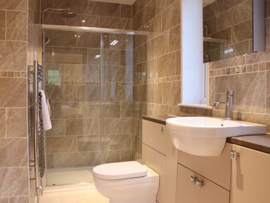 A bathroom with a glass shower enclosure a toilet a sink with a faucet and tiled walls at The Anchorage @ Nables Farm in Upper Seagry