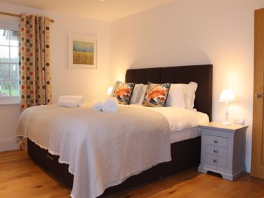 A bedroom with a bed with rolled towels and decorative pillows bedside tables with lamps and a window with curtains at The Anchorage @ Nables Farm in Upper Seagry