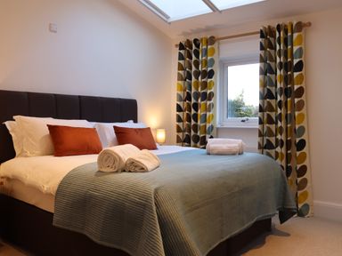 A bedroom with a bed covered with blue bedding white towels and patterned curtains at The Anchorage @ Nables Farm in Upper Seagry