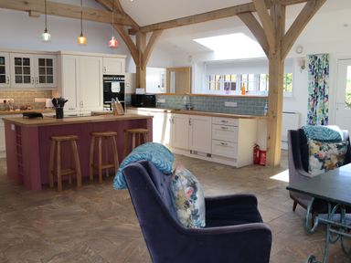 A kitchen with wooden beams and stools around an island with chairs and a table at The Anchorage @ Nables Farm in Upper Seagry