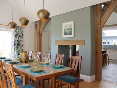 A dining room with a wooden table and chairs with blue cushions three pendant lights and a fireplace at The Anchorage @ Nables Farm in Upper Seagry