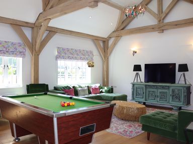 A living room with a pool table green velvet sofas a television on a decorative cabinet and exposed wooden beams at The Anchorage @ Nables Farm in Upper Seagry