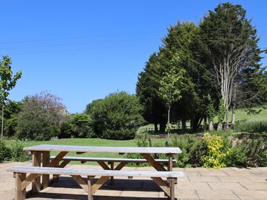 A wooden picnic table on a stone patio with trees and bushes in the background at The Anchorage @ Nables Farm in Upper Seagry