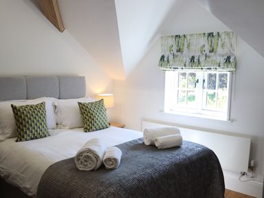 A bedroom with a bed with pillows and rolled towels near a window with a patterned blind at The Anchorage @ Nables Farm in Upper Seagry