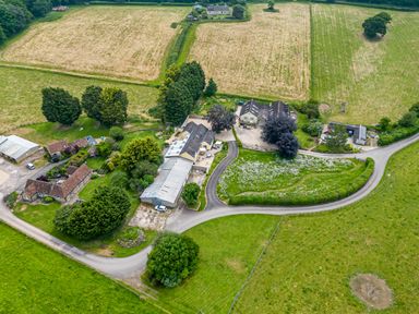 An aerial view of a farm complex with multiple buildings surrounded by fields and trees at The Anchorage @ Nables Farm in Upper Seagry