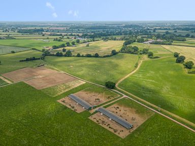 An aerial view of green fields with two long barns and surrounding farmland at The Anchorage @ Nables Farm in Upper Seagry