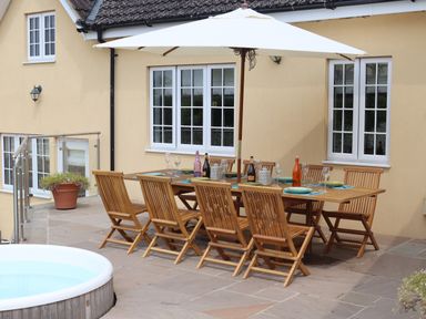 An outdoor dining area with a wooden table and chairs under a white patio umbrella at The Anchorage @ Nables Farm in Upper Seagry