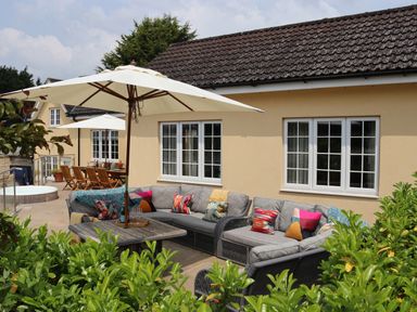An outdoor patio with sofas, a table, umbrellas, and a dining area at The Anchorage @ Nables Farm in Upper Seagry