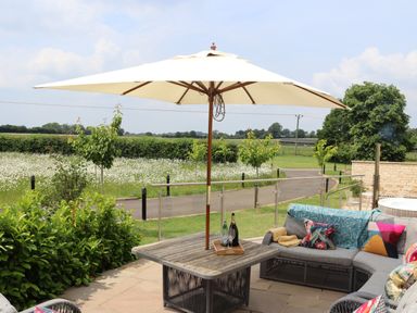 An outdoor patio with table umbrella sofa and cushions overlooking a field of white flowers at The Anchorage @ Nables Farm in Upper Seagry