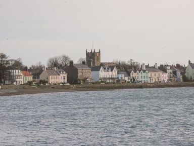 A coastal town with pastel-colored houses and a church tower near the sea at Ty Cuddfan in Llangoed