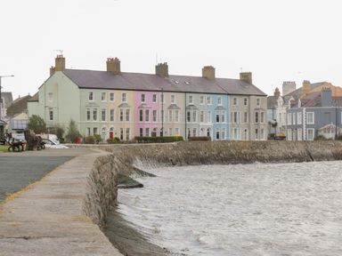 A row of pastel-colored houses along a stone seawall by the water at Ty Cuddfan in Llangoed