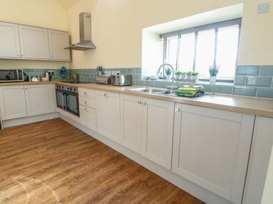 A kitchen with light cabinets an oven microwave sink and toaster on a wooden floor at Ty Cuddfan in Llangoed