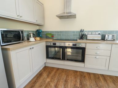 A kitchen with white cabinets wooden countertops a microwave kettle double oven knife set toaster and bread bin at Ty Cuddfan in Llangoed