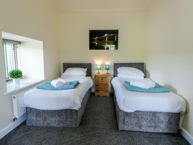 A bedroom with two single beds a wooden nightstand two lamps a window with blinds and a plant at Ty Cuddfan Llangoed