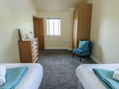 A bedroom with two single beds a wooden chest of drawers a blue chair and a wooden wardrobe at Ty Cuddfan in Llangoed