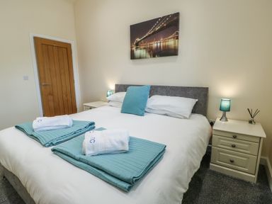 A bedroom with a double bed white and blue bedding two bedside tables with lamps and a door at Ty Cuddfan in Llangoed