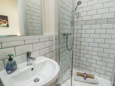 A bathroom with a white sink and a glass shower enclosure with a showerhead at Ty Cuddfan in Llangoed