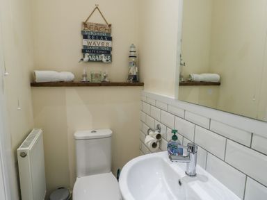 A bathroom with a toilet sink mirror and wall shelf with towels and decorative items at Ty Cuddfan in Llangoed