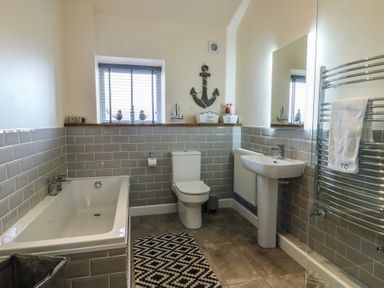 A bathroom with a bathtub toilet sink towel rack and window at Ty Cuddfan in Llangoed