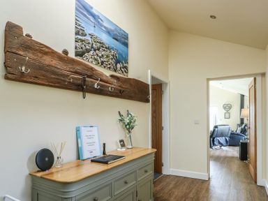 A hallway with a green sideboard and a wooden coat rack with hooks and a coastal picture above it at Ty Cuddfan in Llangoed