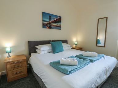 A bedroom with a double bed white bedding blue pillows and blankets wooden bedside tables with lamps and a wall mirror at Ty Cuddfan in Llangoed