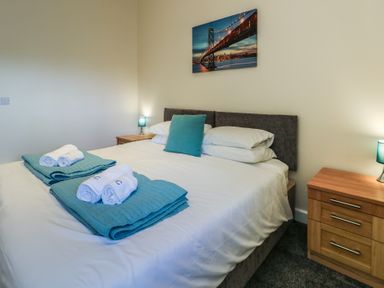 A bedroom with a double bed two folded towels on blue quilts a bedside table with a lamp and a picture of a bridge on the wall at Ty Cuddfan in Llangoed