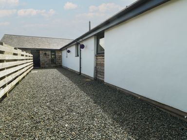 A gravel driveway between a wooden fence and a white building with windows at Ty Cuddfan in Llangoed