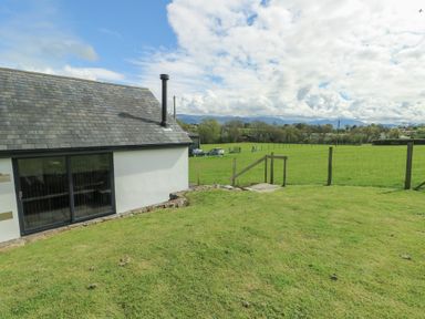 The exterior of a building with a sliding glass door and slate roof next to a fenced green field at Ty Cuddfan in Llangoed