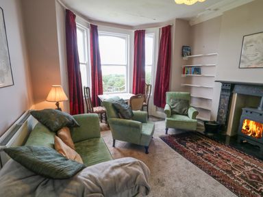 A living room with green sofas a wood burning stove and red curtains at Carriguisnagh in Ballycastle