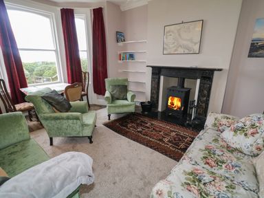 A living room with green armchairs floral sofa wood stove and red curtains at Carriguisnagh Ballycastle