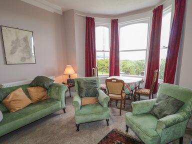 A living room with green sofas and armchairs red curtains and a small dining table with chairs at Carriguisnagh in Ballycastle