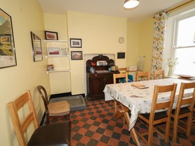 A dining room with wooden chairs around a table with a tablecloth and a dark wood cabinet against a yellow wall at Carriguisnagh in Ballycastle
