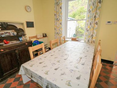 A dining room with a table covered by a bird patterned tablecloth surrounded by wooden chairs and a window with patterned curtains at Carriguisnagh in Ballycastle